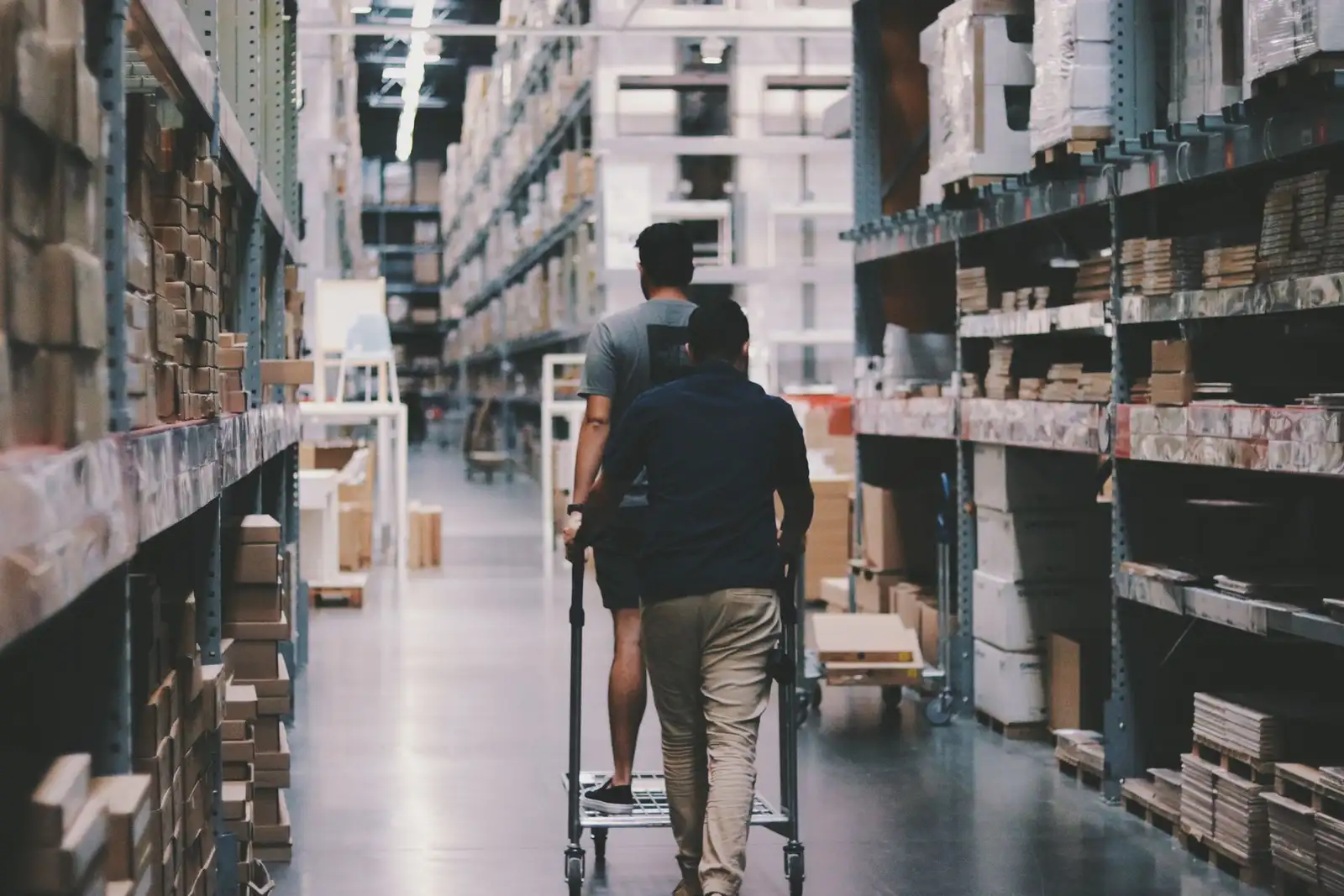 Two workers moving a loaded trolley down a warehouse aisle