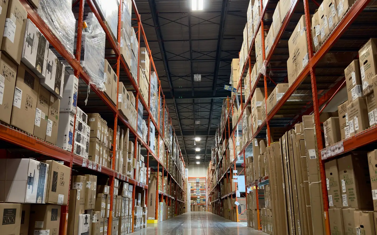 A densely stocked warehouse aisle running into the distance, one worker mid-aisle