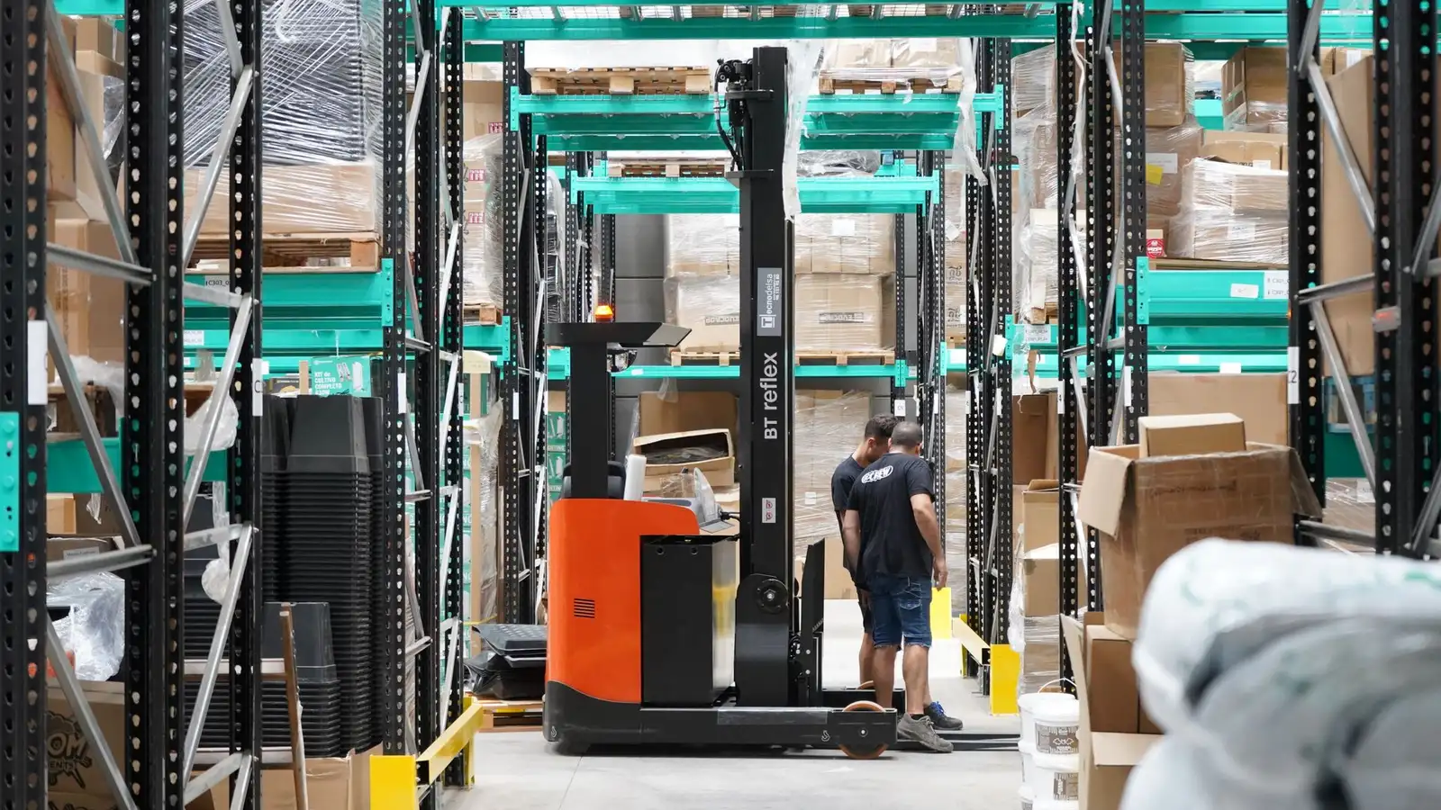 A reach truck and workers operating between warehouse racking