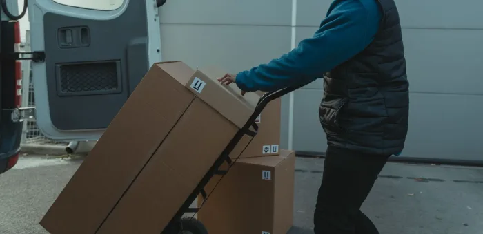 A stacked hand-truck of cartons being pushed to a delivery van
