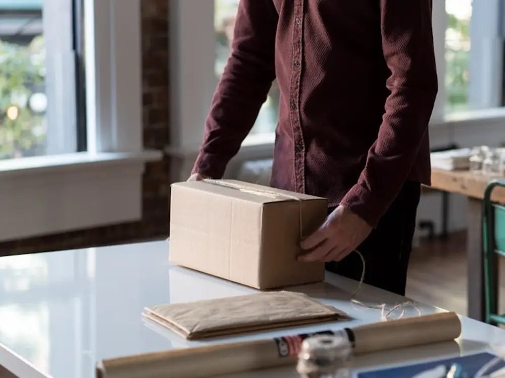 Kraft parcel being tied with twine at a packing bench, paper roll and packing materials in front