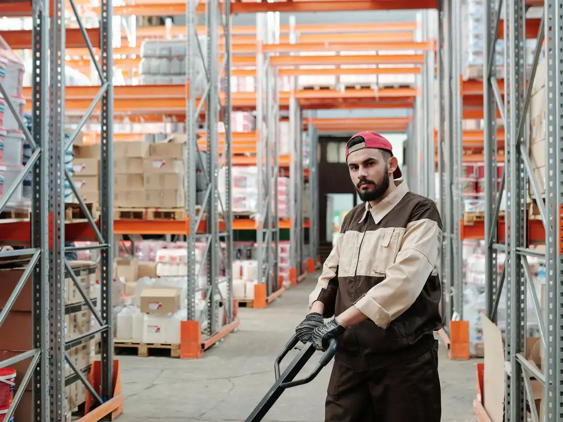 Worker pulling a pallet jack through tall pallet racking